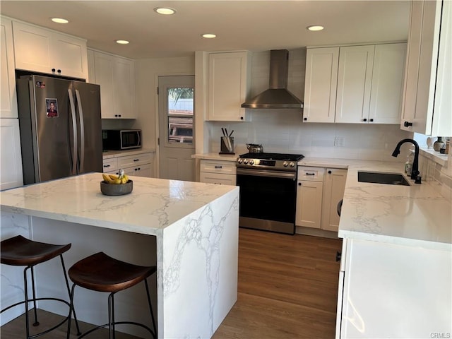 kitchen featuring dark wood-type flooring, a sink, white cabinetry, appliances with stainless steel finishes, and wall chimney range hood