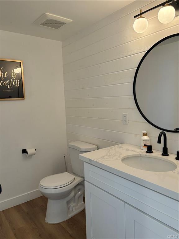 bathroom featuring vanity, wood finished floors, visible vents, baseboards, and toilet