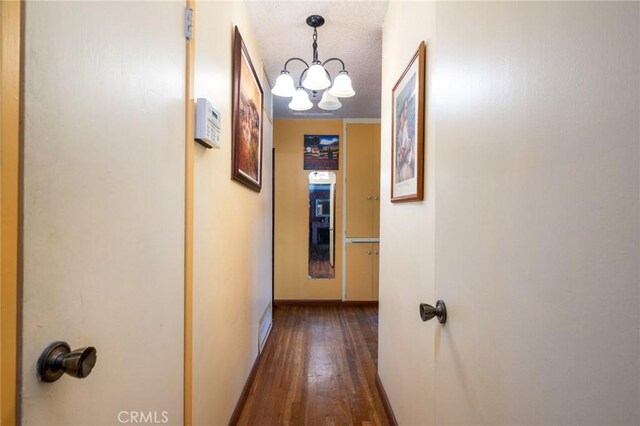 corridor featuring dark wood-style floors, baseboards, a textured ceiling, and a chandelier