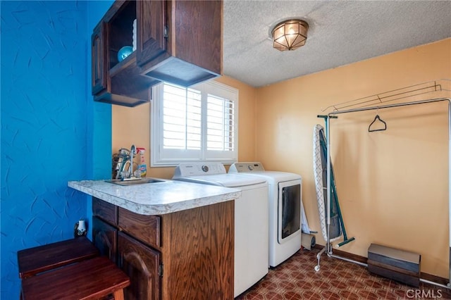 laundry area with baseboards, washing machine and clothes dryer, cabinet space, a sink, and a textured ceiling