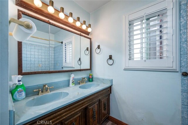 bathroom with double vanity, walk in shower, baseboards, and a sink