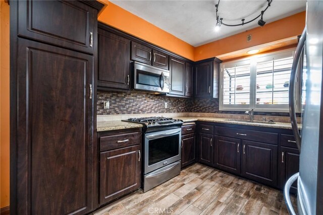 kitchen featuring light wood-style flooring, a sink, stainless steel appliances, dark brown cabinets, and backsplash