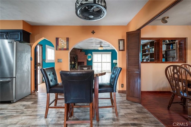 dining room featuring ceiling fan, wood finished floors, arched walkways, and baseboards