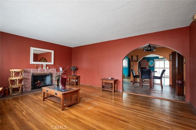 living room featuring a brick fireplace, wood finished floors, arched walkways, and a textured ceiling