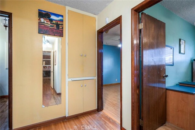 hall featuring a textured ceiling, light wood-type flooring, and baseboards