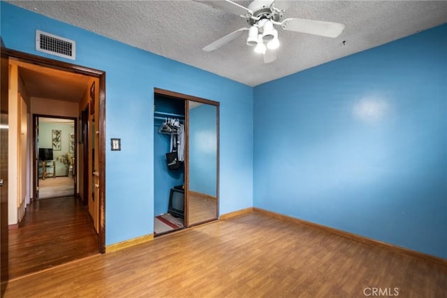 unfurnished bedroom featuring visible vents, a textured ceiling, a closet, and wood finished floors