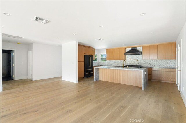 kitchen featuring visible vents, light countertops, modern cabinets, wall chimney exhaust hood, and a kitchen island with sink