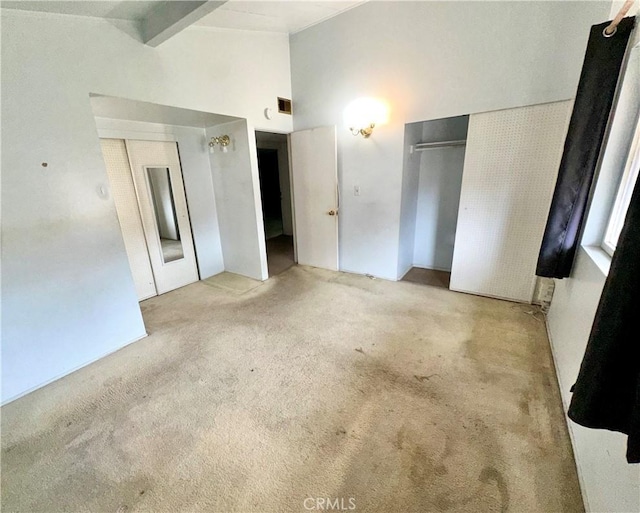 unfurnished bedroom featuring a closet, beam ceiling, carpet, and high vaulted ceiling