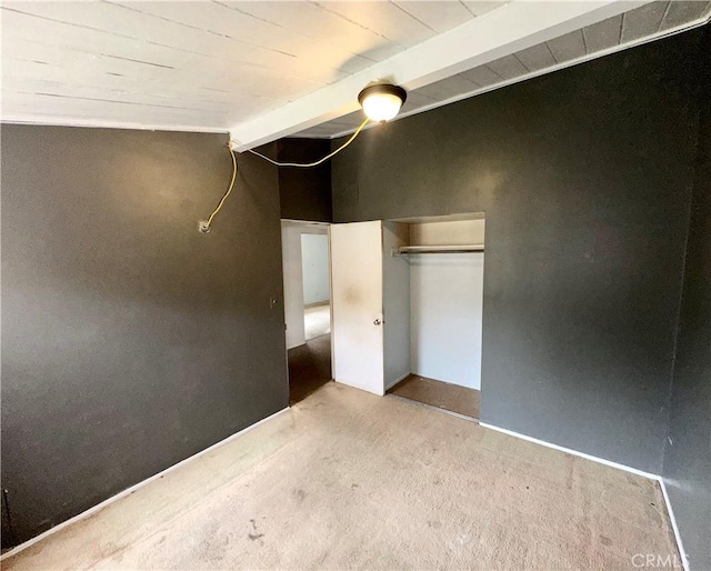 unfurnished bedroom featuring lofted ceiling with beams, a closet, carpet floors, and baseboards