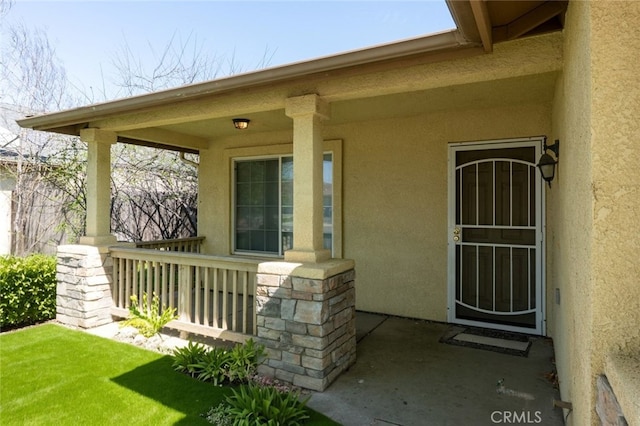 entrance to property with stucco siding, stone siding, and a porch