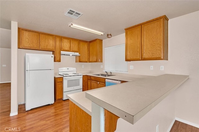 kitchen with white appliances, a peninsula, a sink, light wood-style floors, and under cabinet range hood