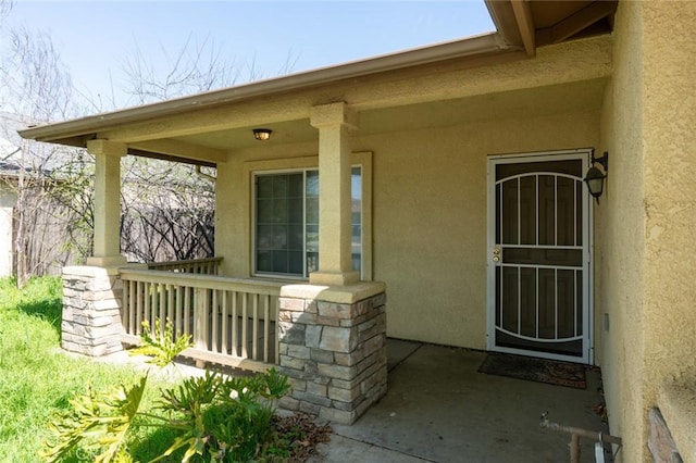 property entrance featuring stone siding, covered porch, and stucco siding