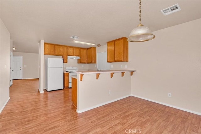 kitchen with visible vents, a kitchen bar, light wood-style flooring, a peninsula, and white appliances