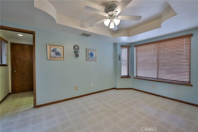 empty room with light carpet, baseboards, a tray ceiling, and a ceiling fan