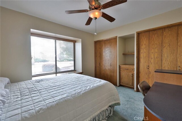 bedroom with two closets, light colored carpet, and ceiling fan