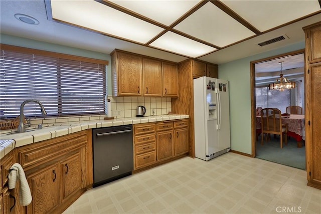 kitchen featuring visible vents, a sink, black dishwasher, white fridge with ice dispenser, and a notable chandelier