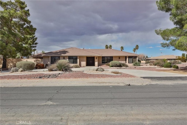 ranch-style house with stucco siding, a tiled roof, concrete driveway, and fence