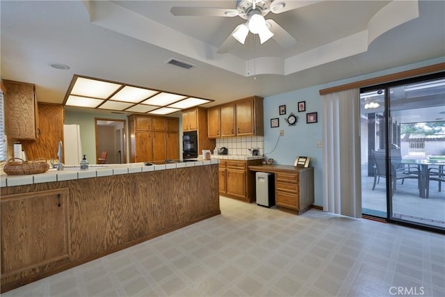 kitchen with tile countertops, visible vents, a tray ceiling, brown cabinets, and backsplash