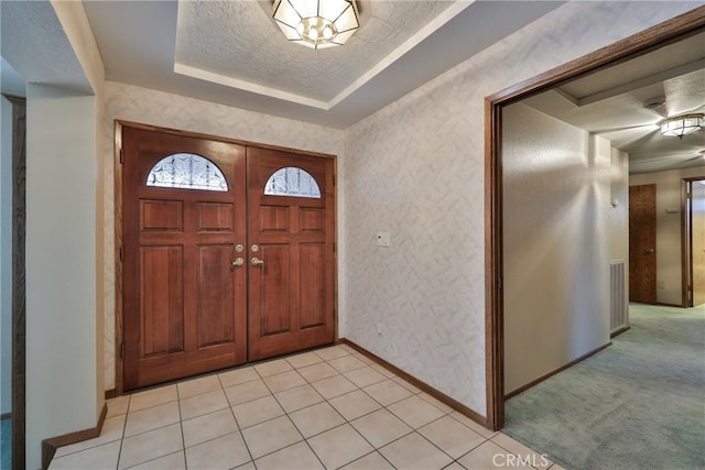 entrance foyer with wallpapered walls, baseboards, light colored carpet, a textured ceiling, and a raised ceiling