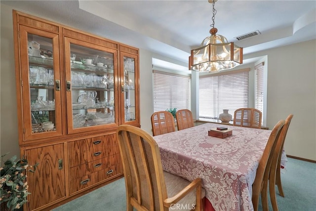 carpeted dining area featuring a tray ceiling, visible vents, baseboards, and a notable chandelier