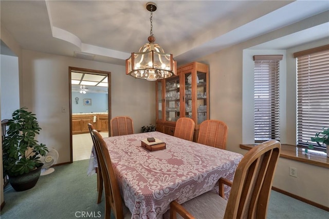 dining room with baseboards, visible vents, carpet floors, a tray ceiling, and a notable chandelier