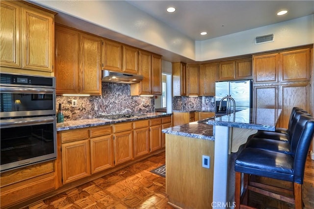 1412 San Clemente Cir, Corona, CA 92882 - kitchen featuring a kitchen breakfast bar, under cabinet range hood, brown cabinets, tasteful backsplash, and stainless steel appliances