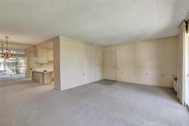 unfurnished living room with a textured ceiling, a notable chandelier, and light carpet