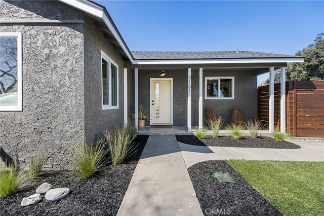 view of exterior entry featuring stucco siding, covered porch, and fence