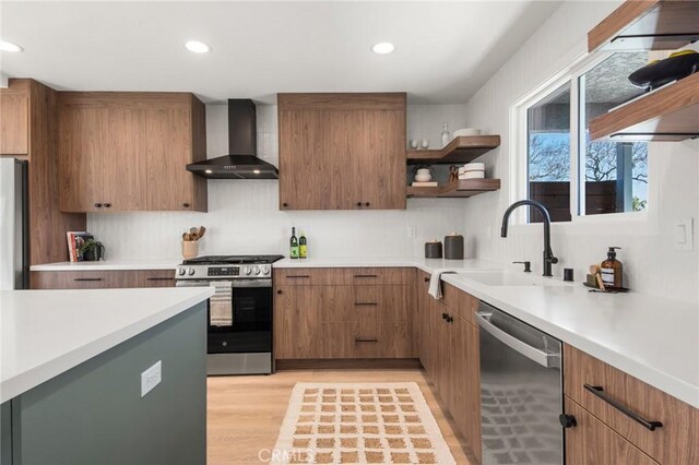 kitchen featuring open shelves, a sink, stainless steel appliances, light countertops, and wall chimney range hood