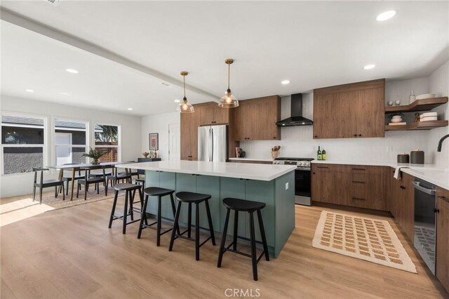 kitchen with a kitchen island, wall chimney range hood, light wood-style flooring, appliances with stainless steel finishes, and open shelves