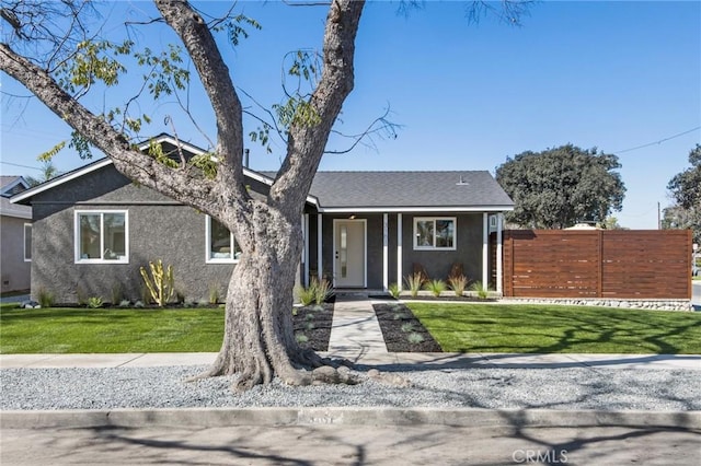 mid-century modern home with a shingled roof, a front yard, fence, and stucco siding