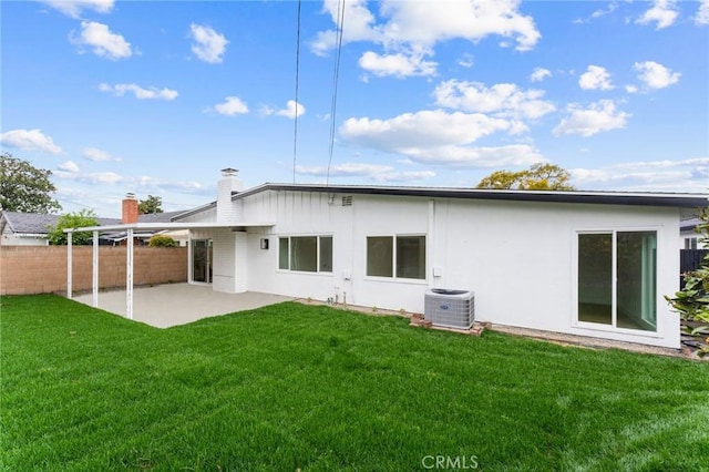 back of property with a lawn, fence, central AC unit, a chimney, and a patio area