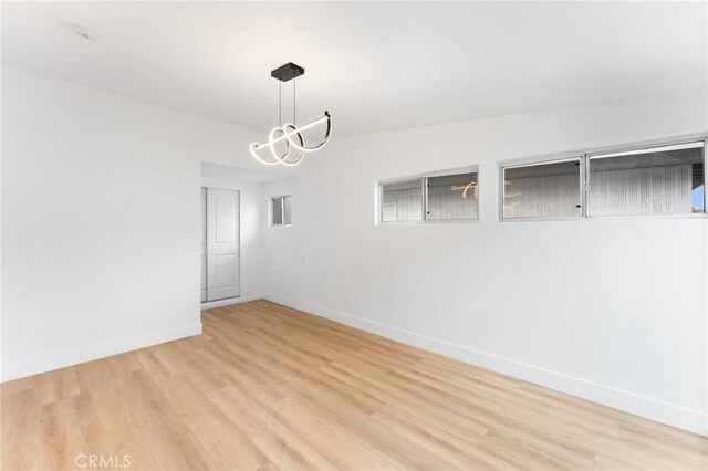 spare room with baseboards, an inviting chandelier, and wood finished floors