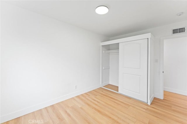 unfurnished bedroom featuring visible vents, baseboards, light wood-style floors, and a closet