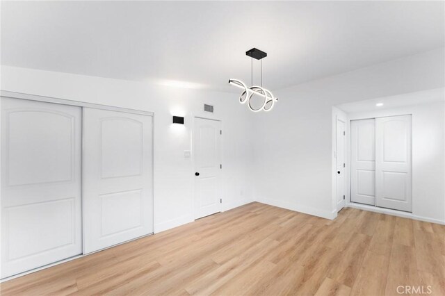 unfurnished dining area with visible vents, baseboards, vaulted ceiling, light wood-style floors, and a notable chandelier