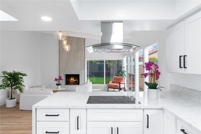 kitchen with black electric stovetop, open floor plan, light stone counters, a peninsula, and island range hood