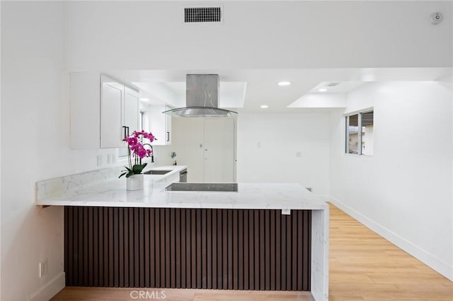 kitchen with light stone counters, ventilation hood, a peninsula, light wood finished floors, and black electric cooktop