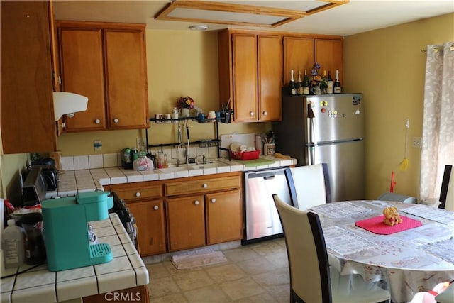 kitchen featuring a sink, stainless steel appliances, brown cabinets, and tile counters