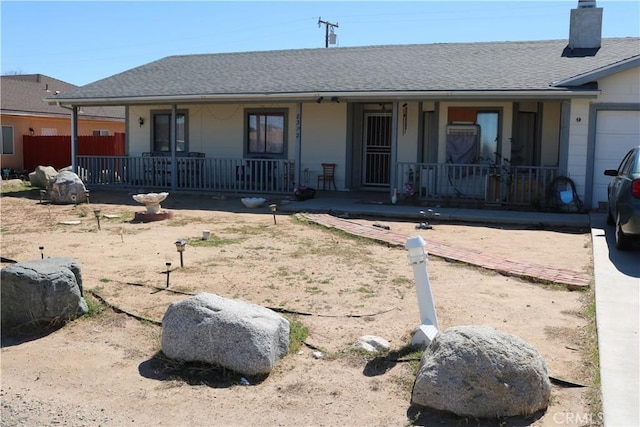 ranch-style home with an attached garage, covered porch, roof with shingles, and a chimney