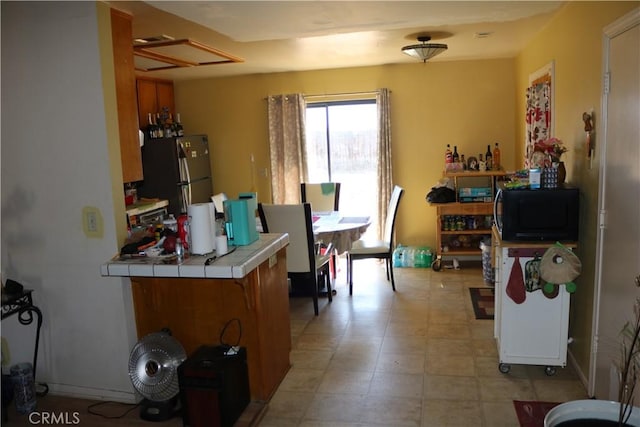 kitchen with a peninsula, freestanding refrigerator, black microwave, and tile counters