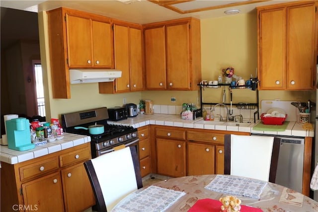 kitchen featuring under cabinet range hood, stainless steel range with gas stovetop, brown cabinetry, and a sink