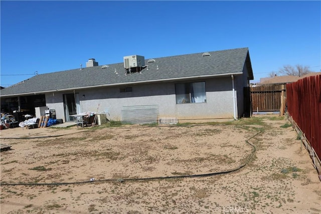 rear view of property featuring a shingled roof, central air condition unit, fence, and stucco siding