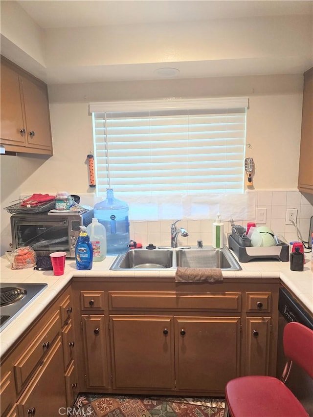 kitchen featuring a sink, tasteful backsplash, stainless steel electric stovetop, light countertops, and dishwashing machine