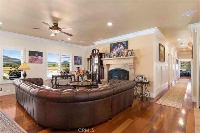 living room featuring a glass covered fireplace, recessed lighting, wood-type flooring, crown molding, and baseboards