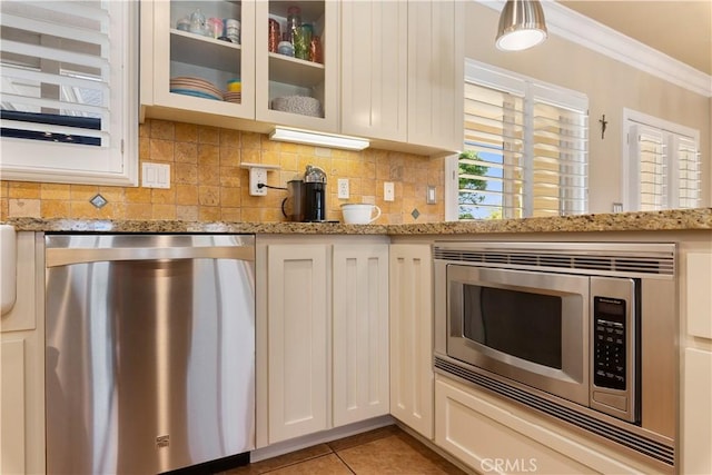 kitchen featuring backsplash, glass insert cabinets, ornamental molding, light tile patterned flooring, and stainless steel appliances