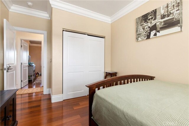 bedroom featuring a closet, ornamental molding, baseboards, and wood finished floors