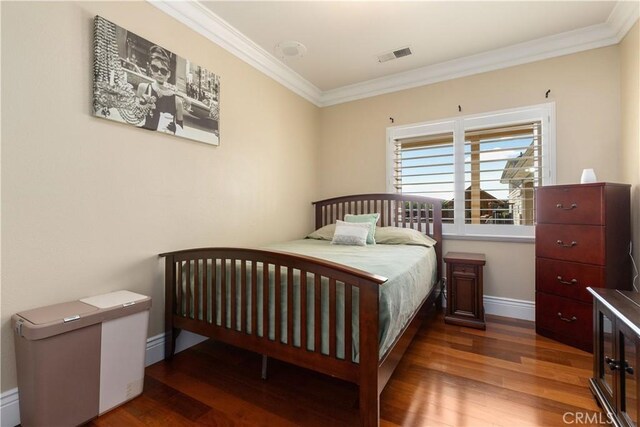 bedroom featuring baseboards, wood finished floors, visible vents, and ornamental molding