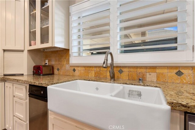 kitchen featuring a sink, light stone counters, backsplash, white cabinetry, and glass insert cabinets