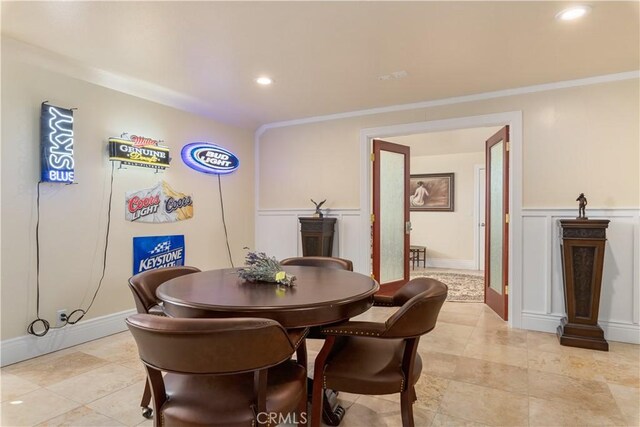 dining space featuring a decorative wall, crown molding, and a wainscoted wall