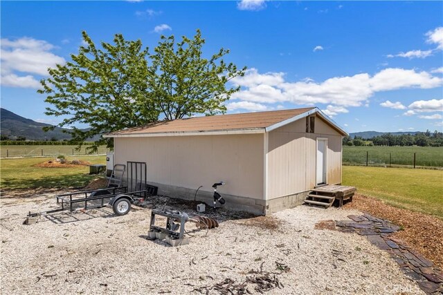 view of home's exterior with an outdoor structure, a rural view, a mountain view, and a lawn